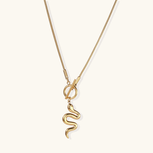 Gold-plated stainless steel necklace with curved serpent pendant on delicate chain against cream background.