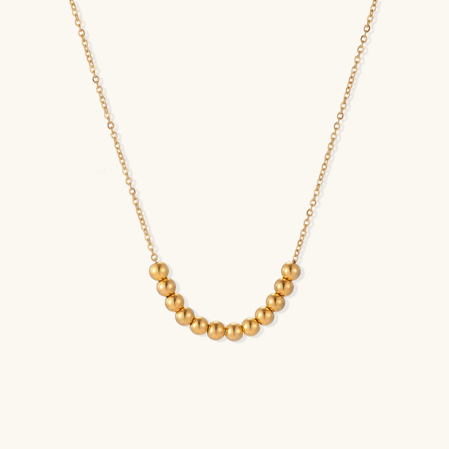Delicate gold-plated chain necklace featuring clustered spherical beads arranged in elegant curve against white background.