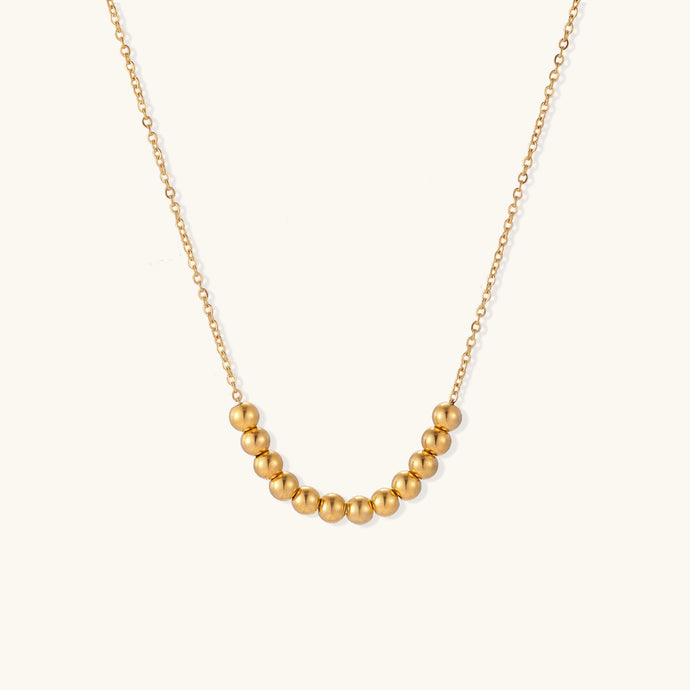 Delicate gold-plated chain necklace featuring clustered spherical beads arranged in elegant curve against white background.