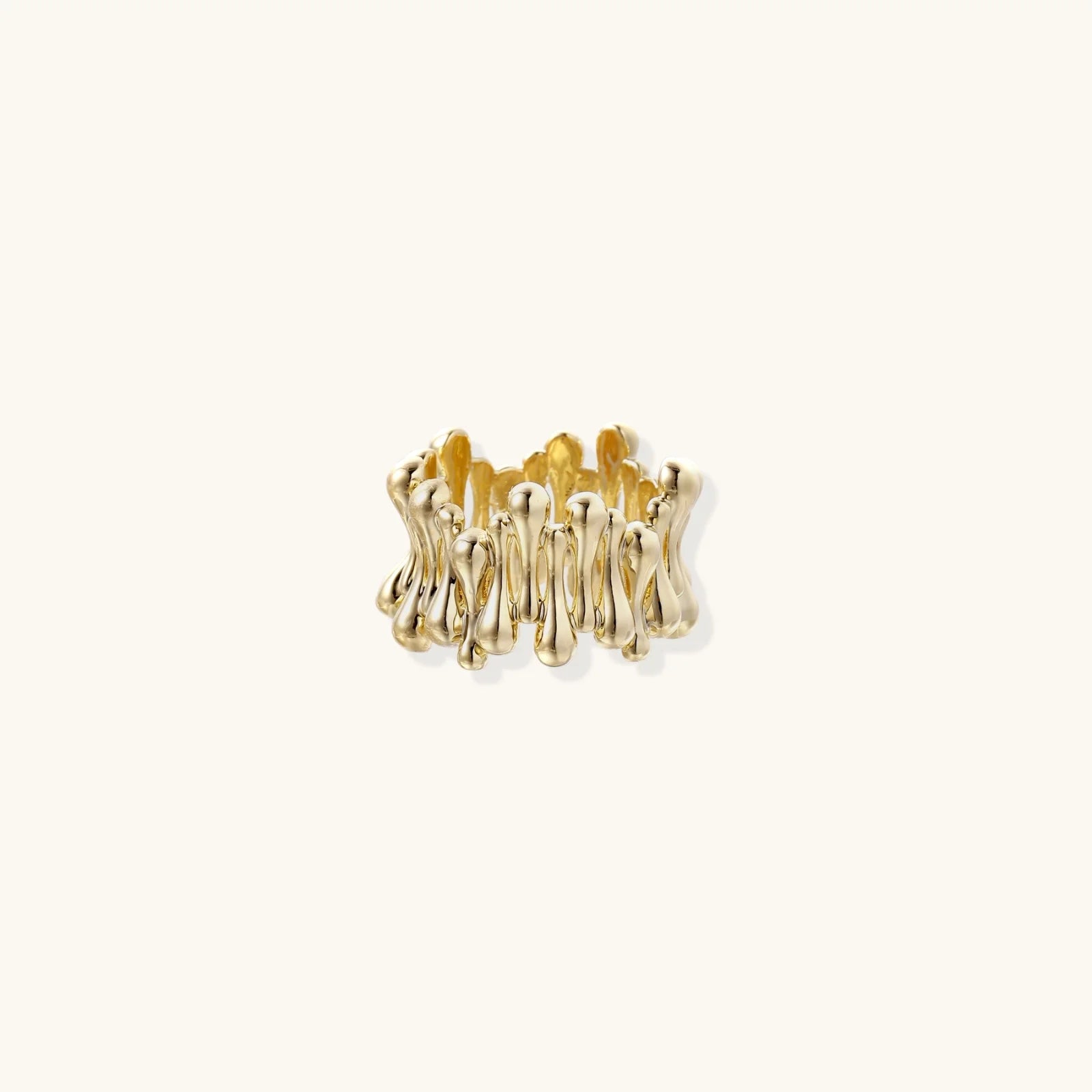 Gold-plated brass ring with sculptural petal-like elements in a wide band design on beige background