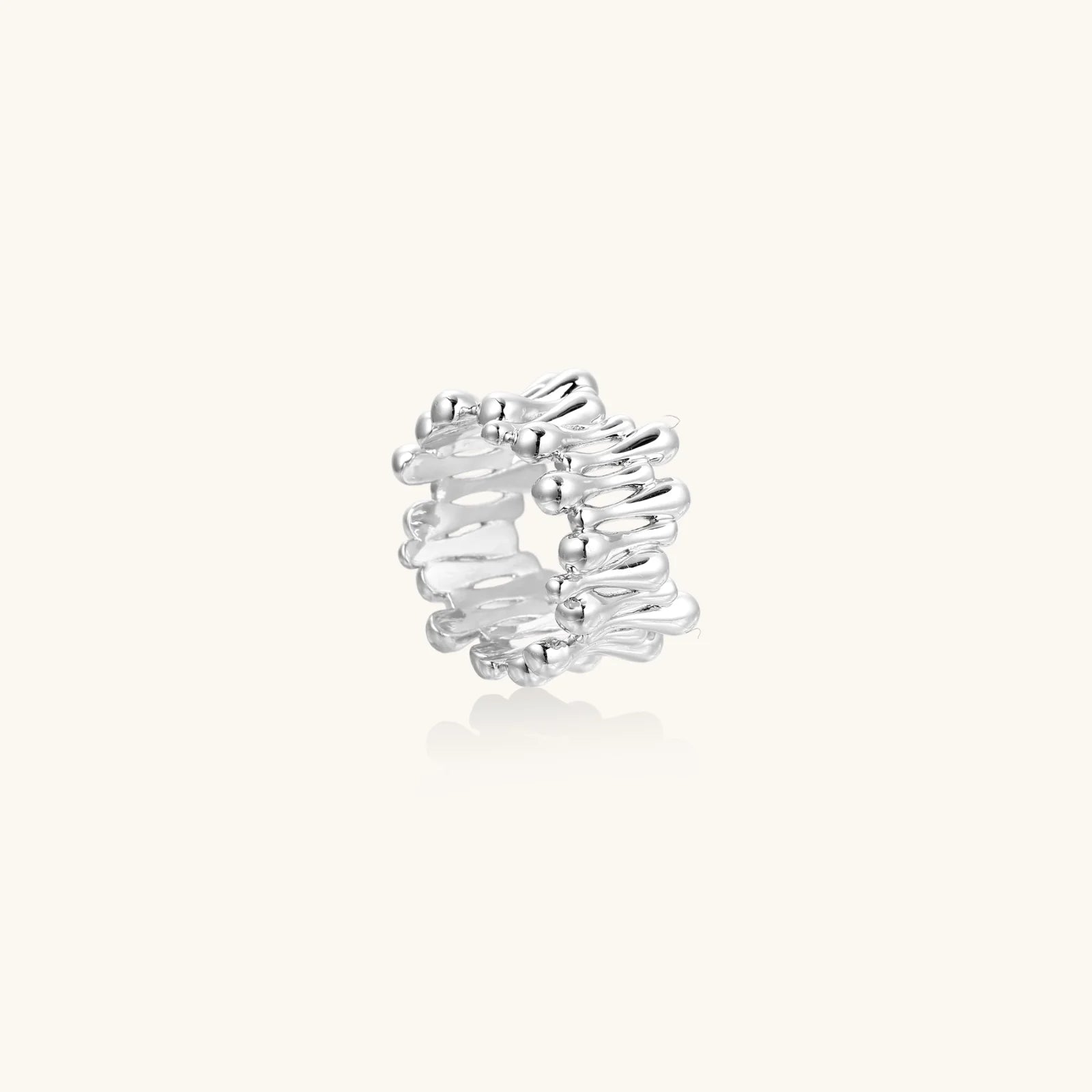 Wide band ring with sculptural wave ripples in polished white gold plated eco-brass on cream background