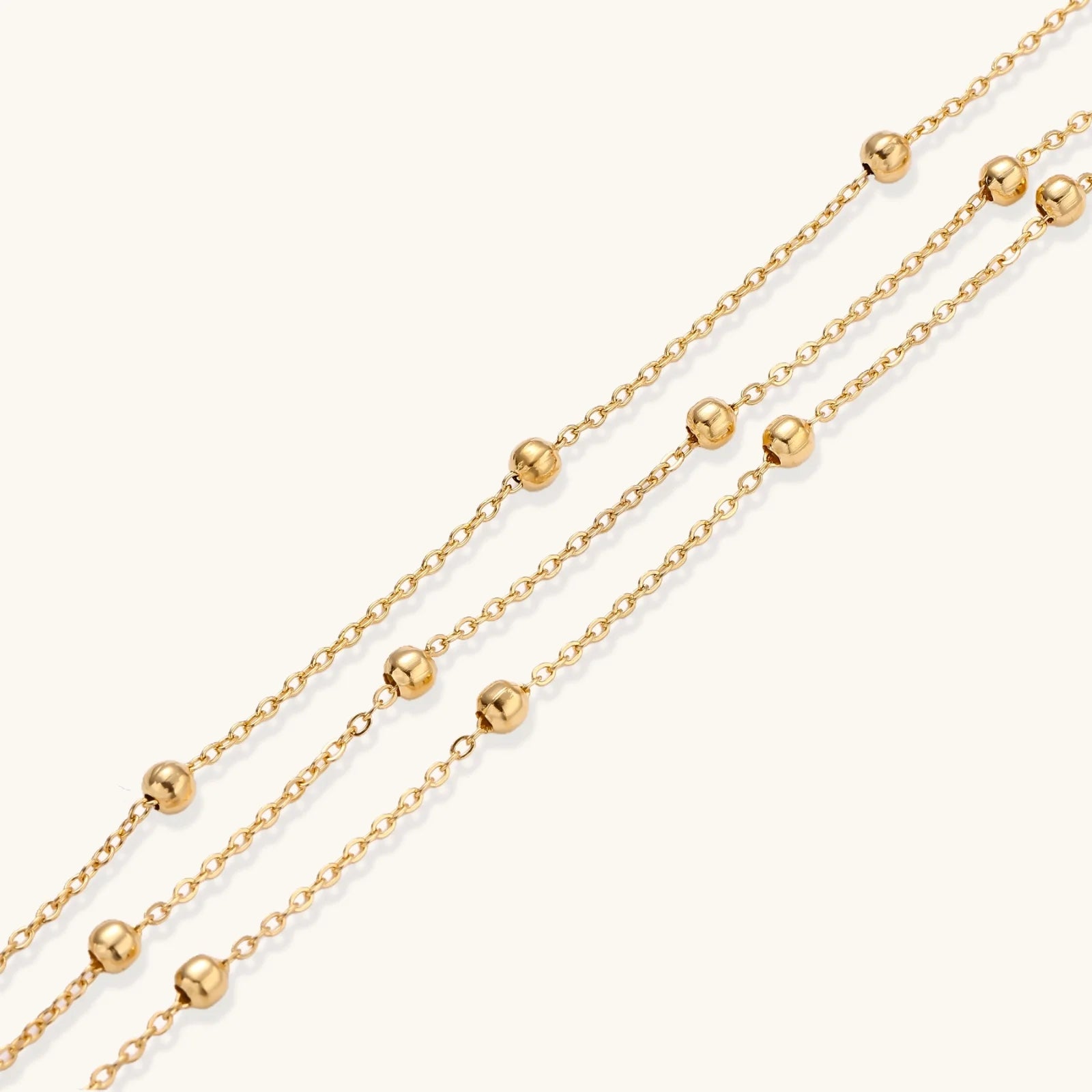Three-strand gold-plated bracelet with clustered ball beads and adjustable clasp on cream background